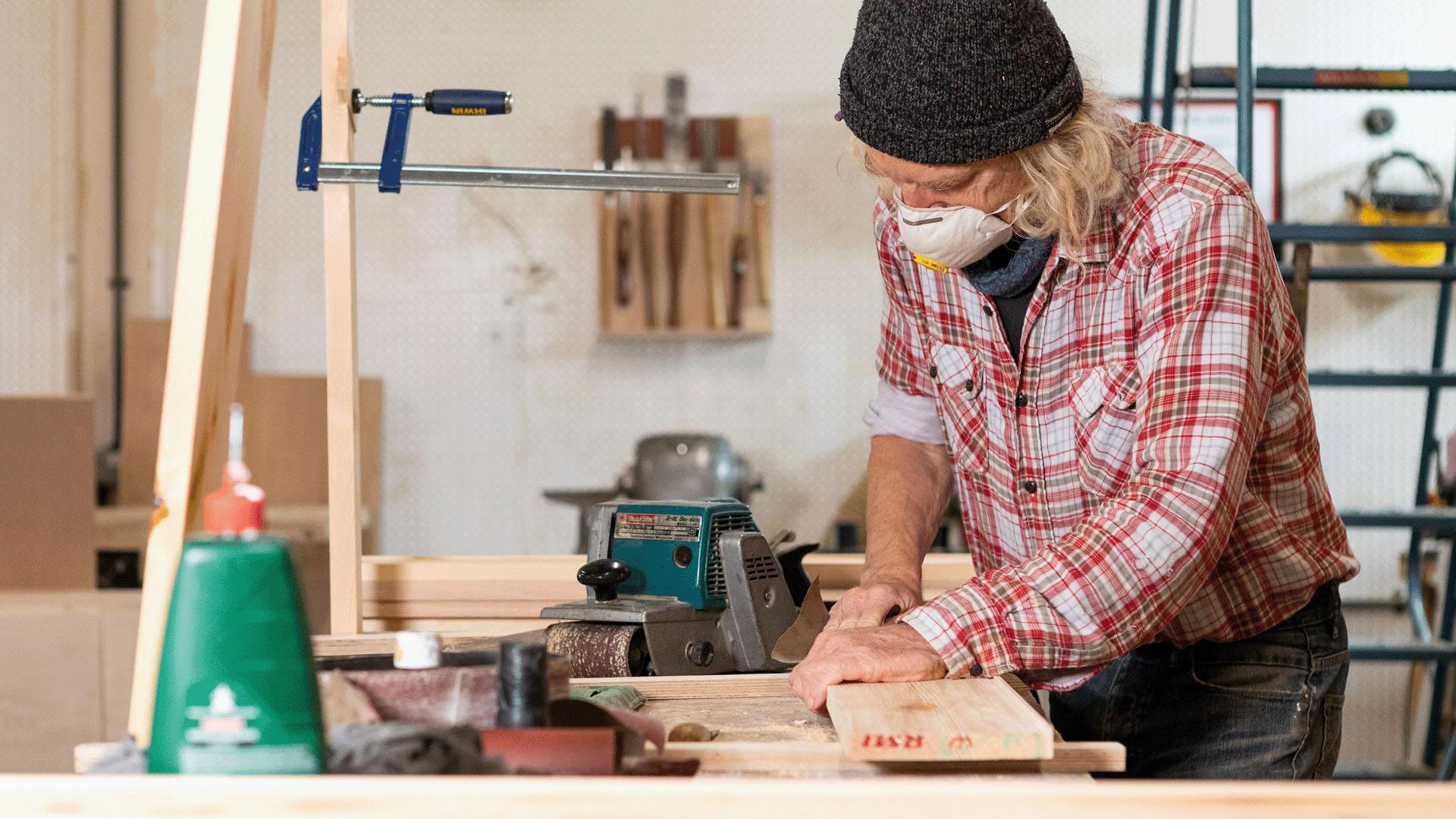 Older man with hat and dust mask working on a bench