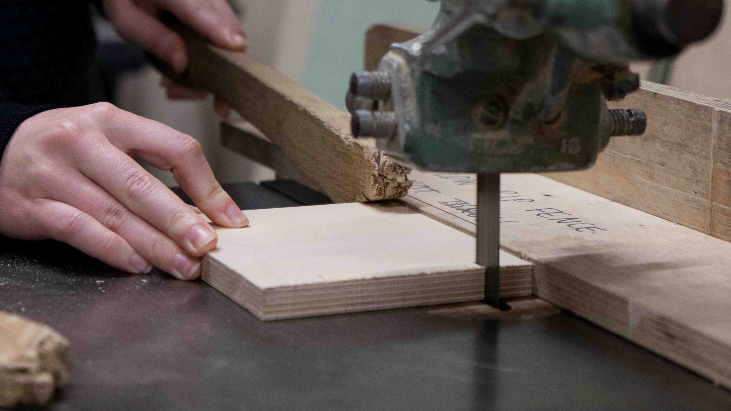Hands cutting a piece of wood on bandsaw using push sticks