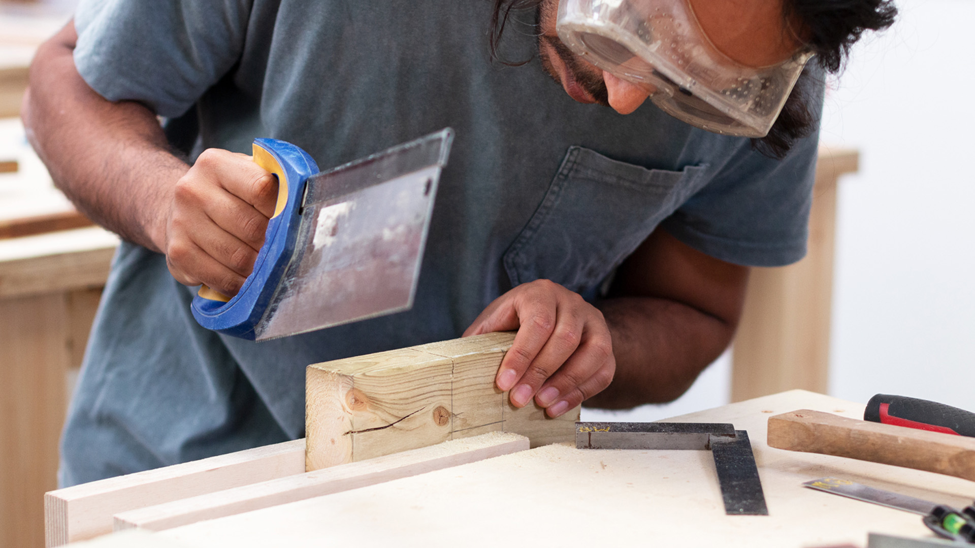 Man with goggles using a handsaw to cut wood