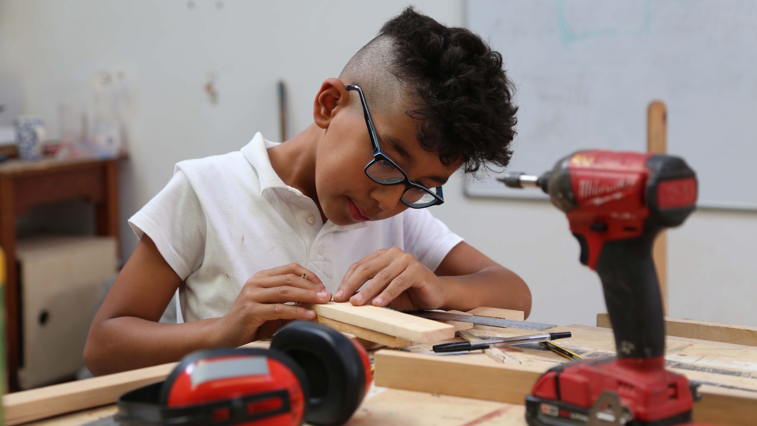 Boy marking out wood project wearing glasses