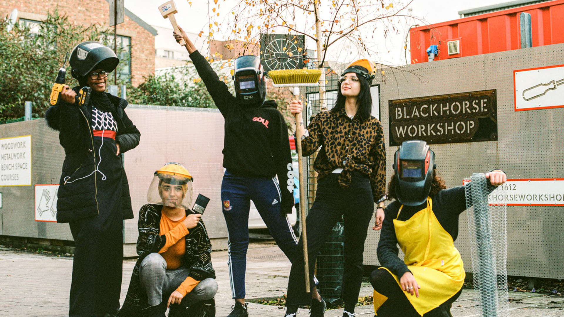 Young people posing with tools such as drill