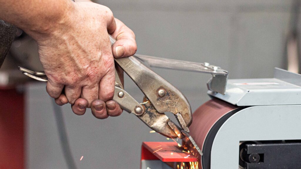 Pliers holding metal over a metal belt sander